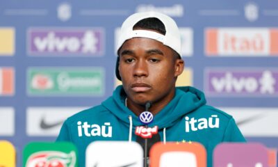 Jovem jogador Endrick em coletiva de imprensa, usando boné branco e moletom teal com logos de patrocinadores