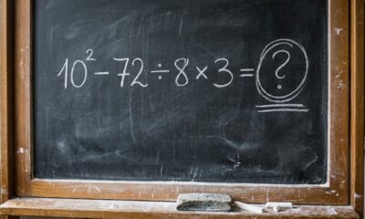 Quadro-negro com a expressão matemática 10² − 72 ÷ 8 × 3 escrita em giz e um ponto de interrogação, sem mostrar o resultado.