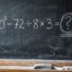 Quadro-negro com a expressão matemática 10² − 72 ÷ 8 × 3 escrita em giz e um ponto de interrogação, sem mostrar o resultado.