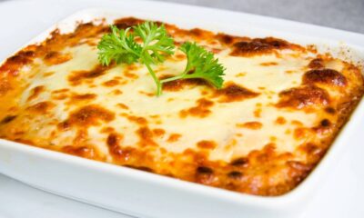 Lasanha em refratário branco, com queijo gratinado e dourado, decorada com um raminho de salsinha