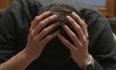 Homem com as mãos na cabeça e a cabeça baixa, vestindo um suéter cinza e relógio