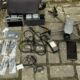 Drone cinza, controle remoto, baterias, hélices lacradas, cabos e celular preto em piso de concreto