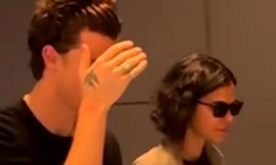 Shawn Mendes com a mão no rosto, ao lado de Bruna Marquezine de óculos escuros