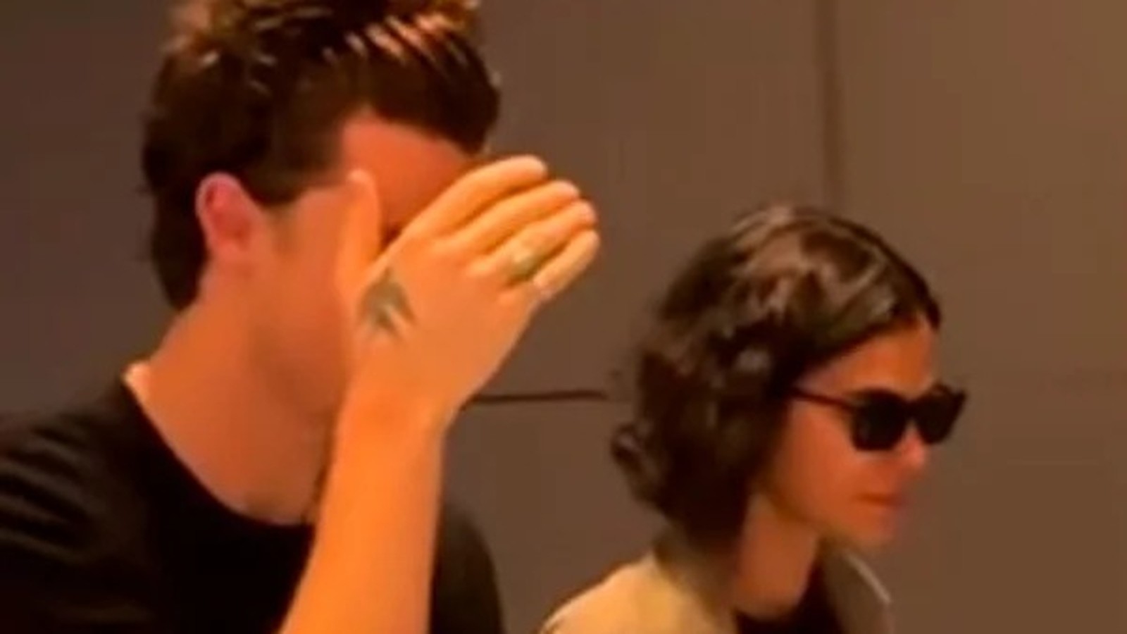 Shawn Mendes com a mão no rosto, ao lado de Bruna Marquezine de óculos escuros