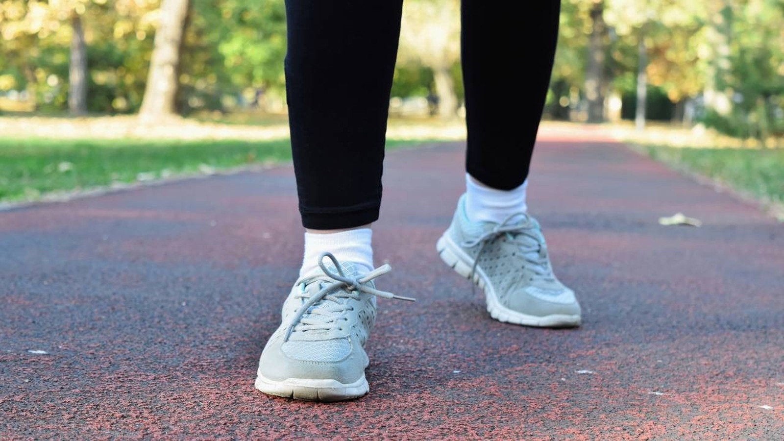 Pernas de pessoa com tênis cinza e calças pretas caminhando em pista de corrida