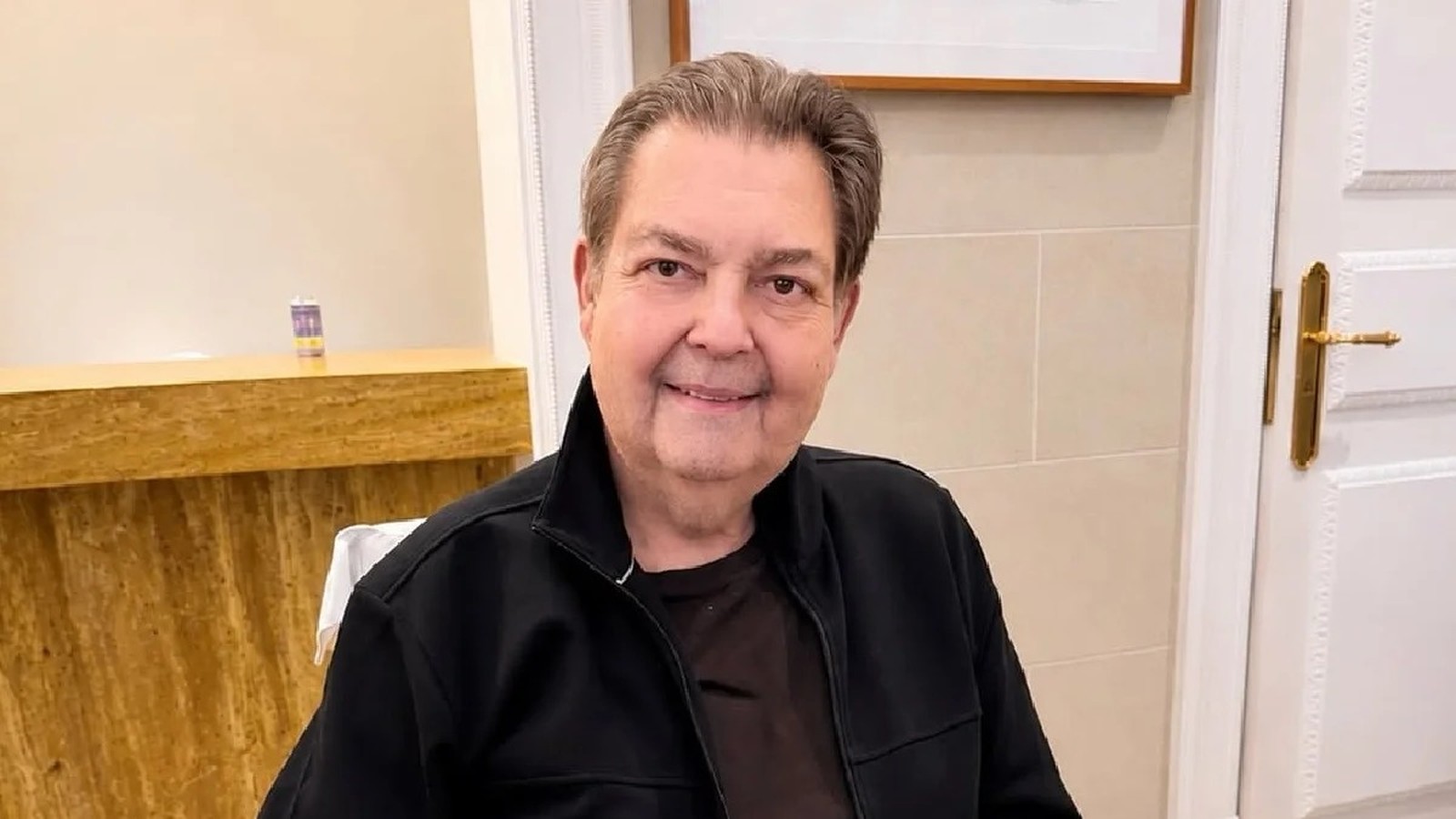 Homem de meia-idade, Faustão, sorrindo e olhando para a câmera, vestindo jaqueta preta.