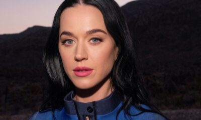 Katy Perry em close-up, cabelo escuro, olhos azuis, batom rosa e jaqueta azul