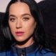 Katy Perry em close-up, cabelo escuro, olhos azuis, batom rosa e jaqueta azul