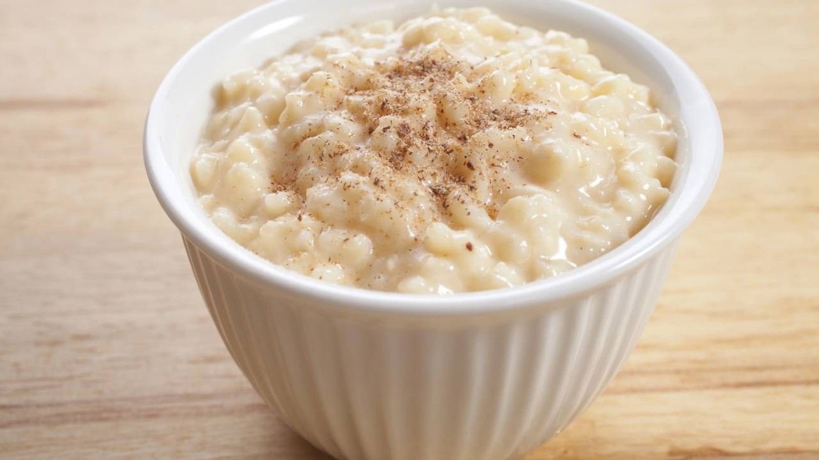 Arroz doce em tigela branca com canela em pó sobre uma superfície de madeira