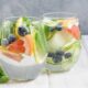 Dois copos de água saborizada com pepino, limão, toranja, mirtilos e hortelã sobre mesa de madeira