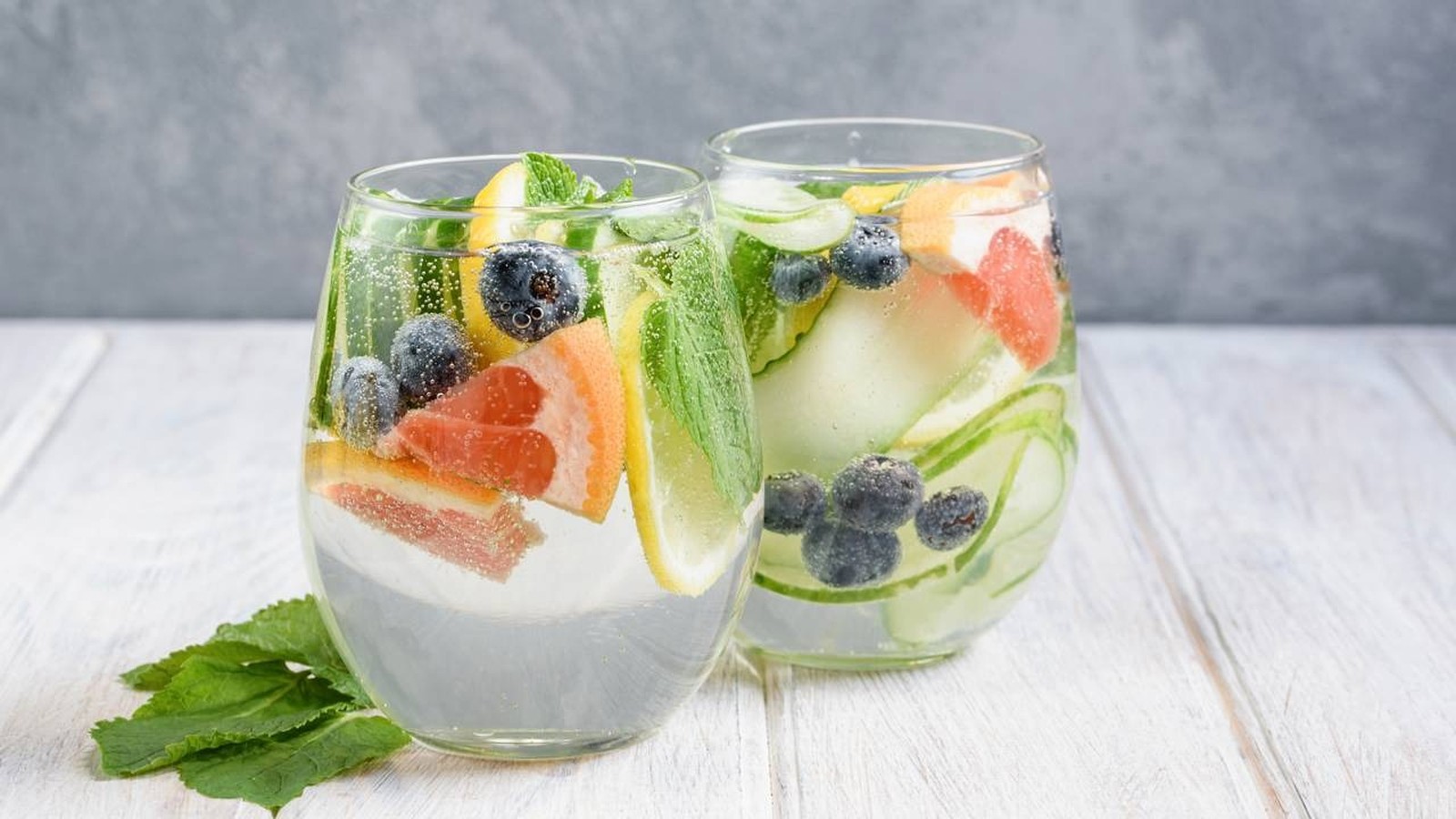 Dois copos de água saborizada com pepino, limão, toranja, mirtilos e hortelã sobre mesa de madeira