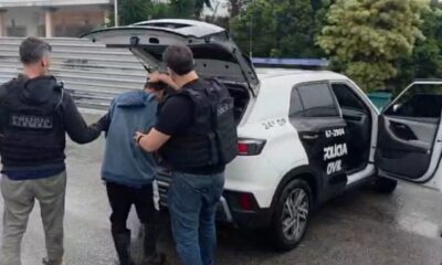 Dois policiais prendem um homem ao lado de viatura da Polícia Civil, com inscrições 24ª DP