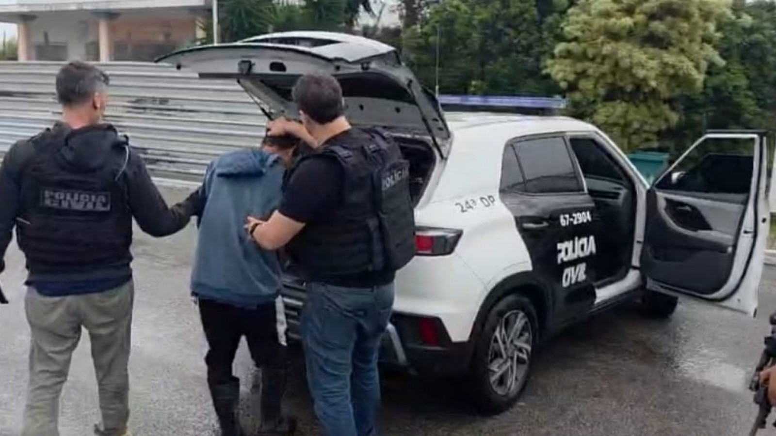 Dois policiais prendem um homem ao lado de viatura da Polícia Civil, com inscrições 24ª DP