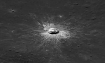 Cratera de impacto circular no solo lunar cinza, com material ejetado brilhante ao redor