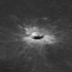 Cratera de impacto circular no solo lunar cinza, com material ejetado brilhante ao redor