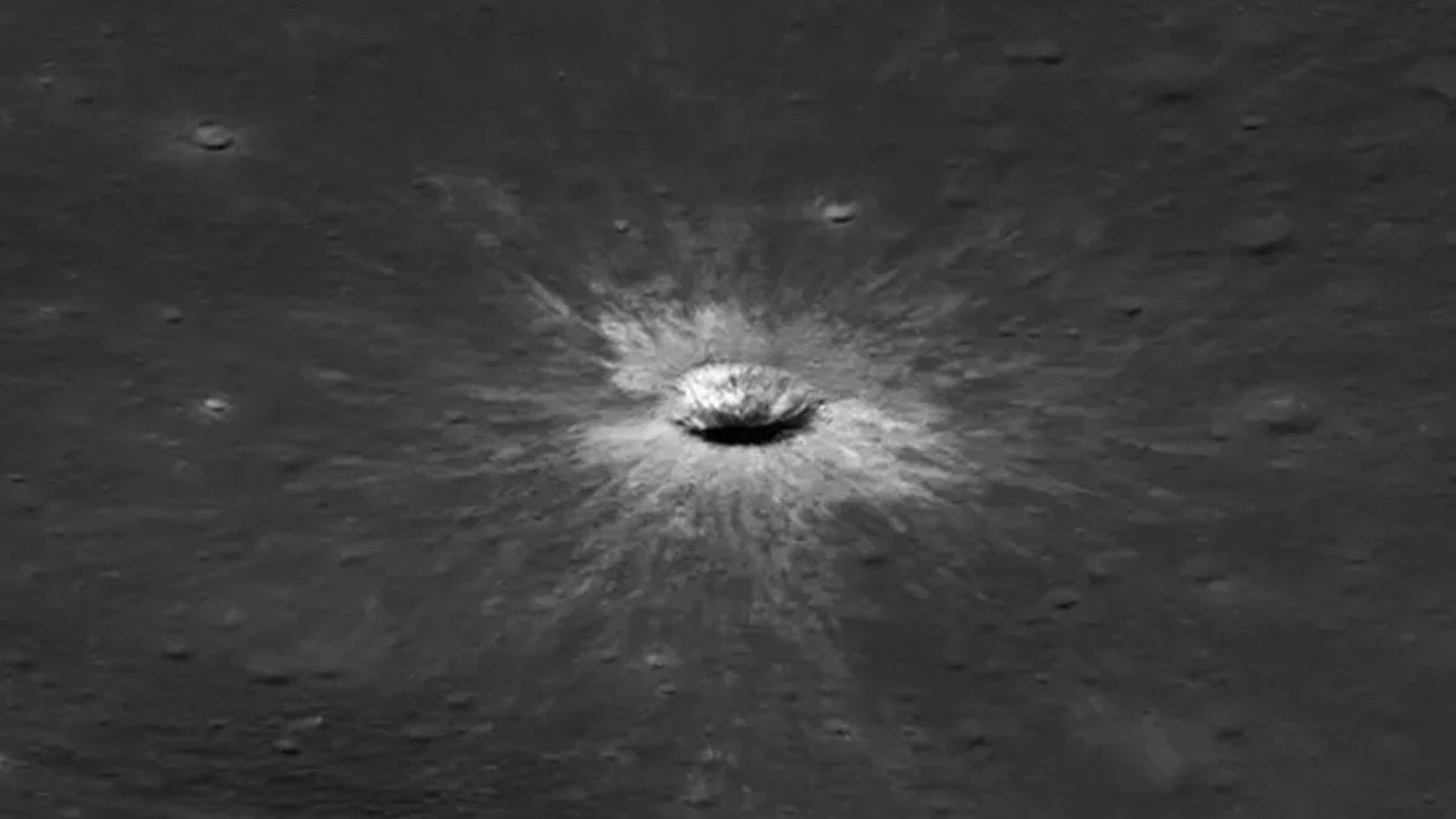 Cratera de impacto circular no solo lunar cinza, com material ejetado brilhante ao redor