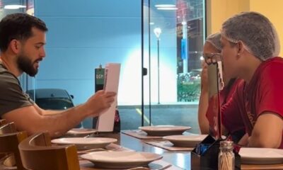 Homem com barba lendo papel para duas mulheres de touca na mesa de um restaurante