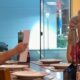 Homem com barba lendo papel para duas mulheres de touca na mesa de um restaurante