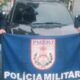 Dois policiais seguram bandeira PMERJ, Polícia Militar, em frente a carro escuro