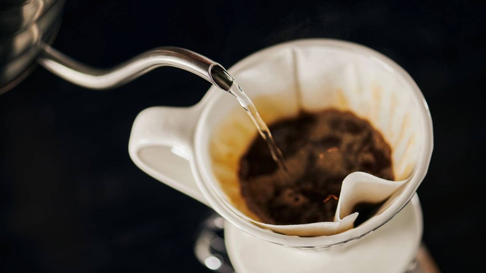 Chaleira despejando água quente sobre pó de café em um filtro de coador branco