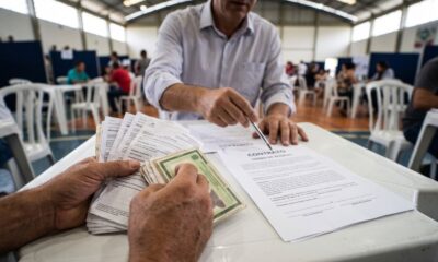 Mãos seguram documentos e RG. Homem aponta para 'CONTRATO TERMO DE ACORDO' em mesa