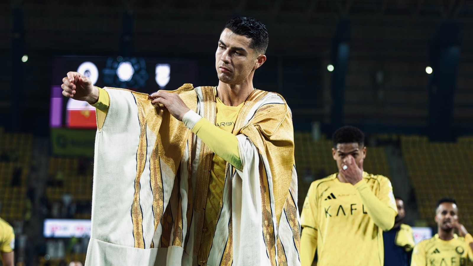 Cristiano Ronaldo, em campo, veste túnica árabe branca e dourada sobre camisa amarela