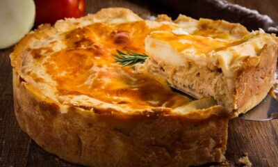 Fatia de empadão de frango dourado sendo retirada de torta inteira com espátula