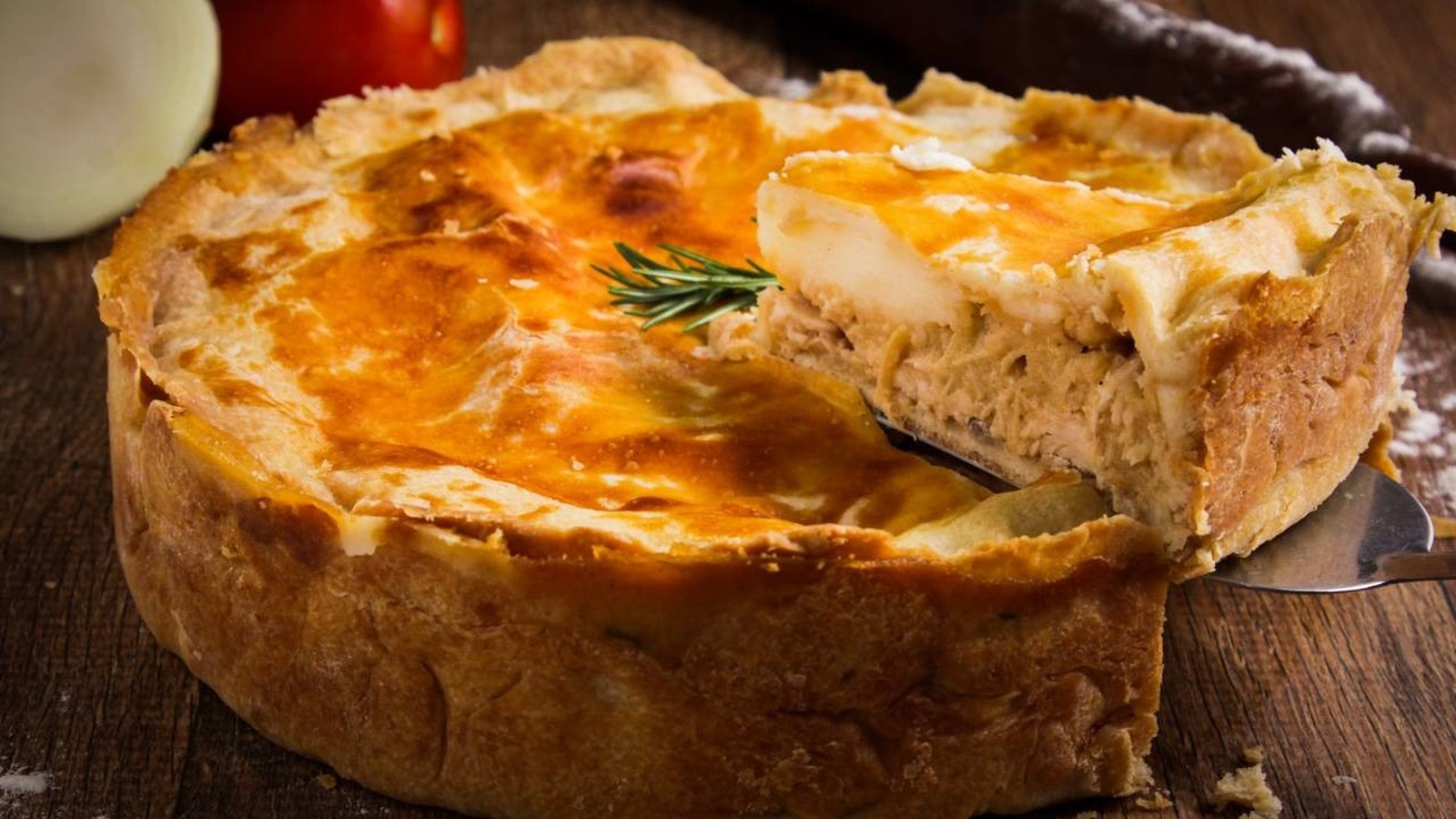 Fatia de empadão de frango dourado sendo retirada de torta inteira com espátula
