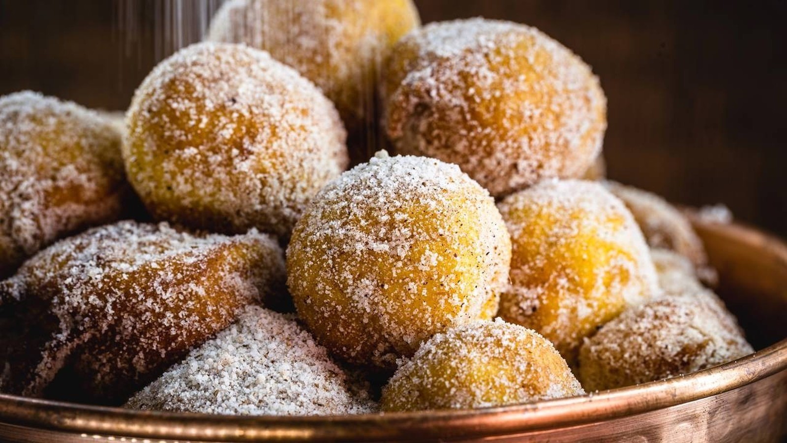 Pilha de bolinhos de chuva dourados e redondos, cobertos por açúcar granulado
