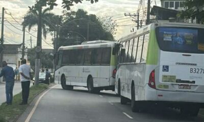 Dois ônibus brancos e verdes parados em uma rua, com homens na calçada
