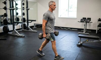 Pessoa com mais de 50 anos caminhando com dois halteres ao lado do corpo e mantendo a postura ereta.