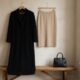 Casaco longo preto ao lado de saia lápis neutra e bolsa preta minimalista, representando um guarda-roupa cápsula de outono inspirado nos anos 90.