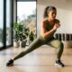 Mulher de cerca de 50 anos fazendo passo lateral com agachamento durante treino de cardio em casa.