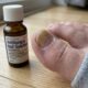 Unha do pé amarelada e espessa ao lado de medicamento antifúngico, com crescimento saudável visível na base.