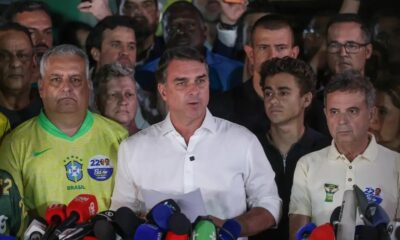 Jair Bolsonaro discursa em pódio com microfones; homens de camisas do Brasil atrás