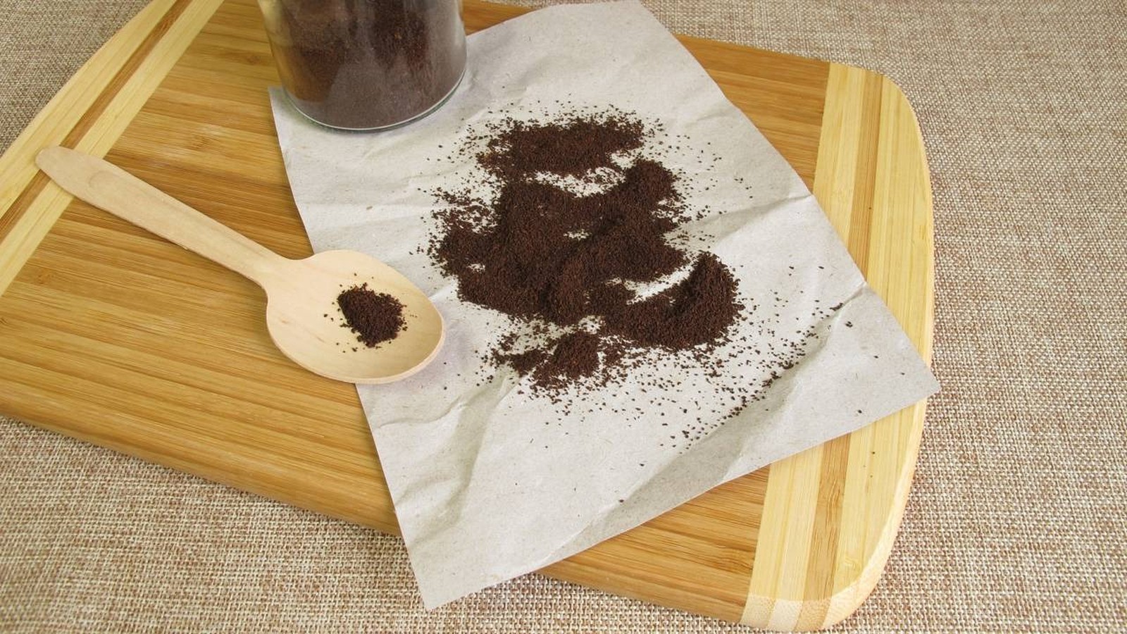 Pó de café espalhado em papel amassado e em uma colher de madeira sobre uma tábua