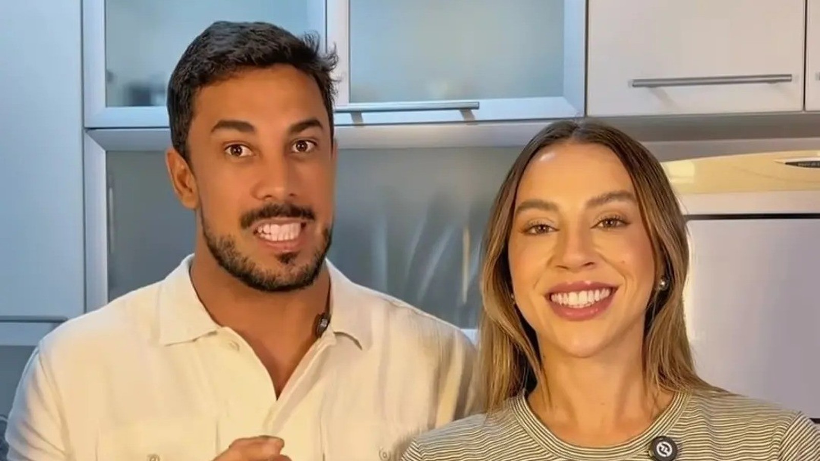 Casal sorridente, homem e mulher, olhando para frente em ambiente interno claro