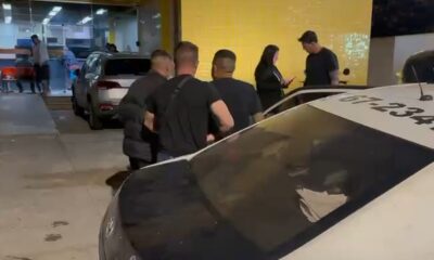 Homens próximos a viatura policial branca com número 67-234 no teto, em operação noturna