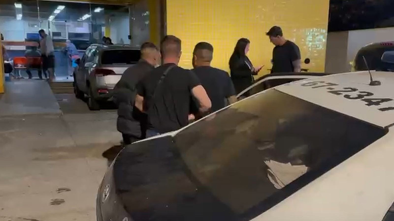 Homens próximos a viatura policial branca com número 67-234 no teto, em operação noturna