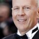 Close-up do ator Bruce Willis, sorrindo, de smoking e gravata borboleta preta
