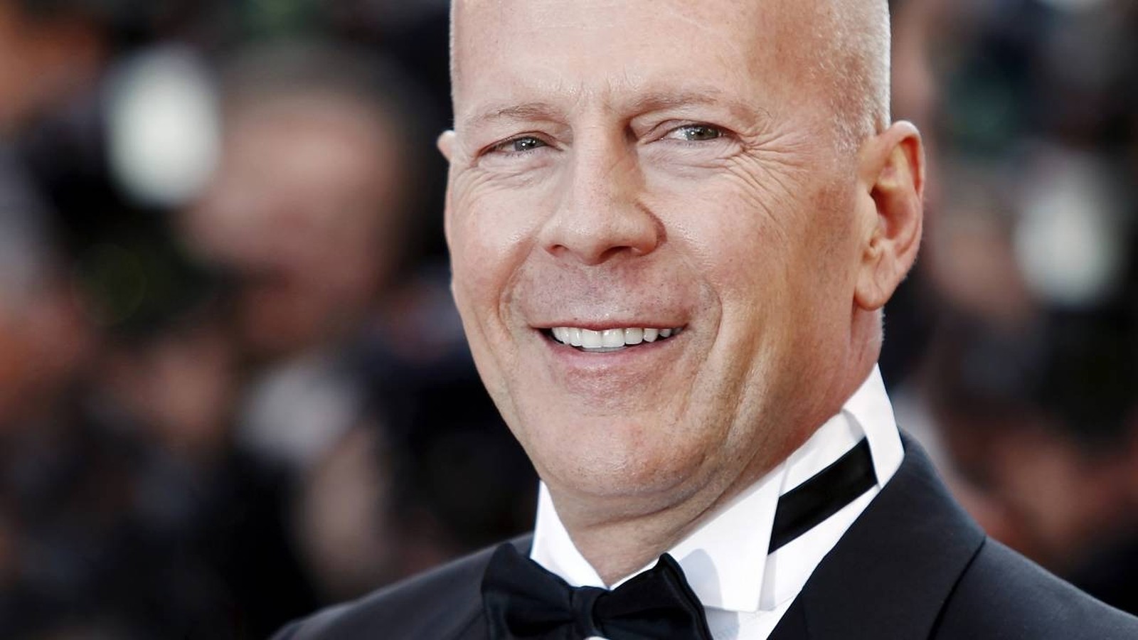 Close-up do ator Bruce Willis, sorrindo, de smoking e gravata borboleta preta