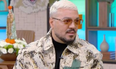 Homem de cabelo loiro platinado, barba, óculos de sol e jaqueta estampada olhando à direita
