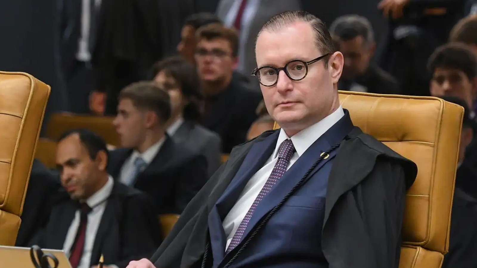Ministro Cristiano Zanin, de óculos e toga, sentado em cadeira de couro
