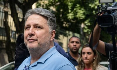 Homem com cabelo grisalho, camisa polo azul, óculos no colarinho, em meio a equipe de filmagem
