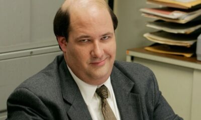 Homem careca, Brian Baumgartner, de terno, sorri maliciosamente em escritório