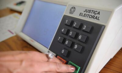 Mão pressiona o botão verde 'CONFIRMA' de uma urna eletrônica da Justiça Eleitoral