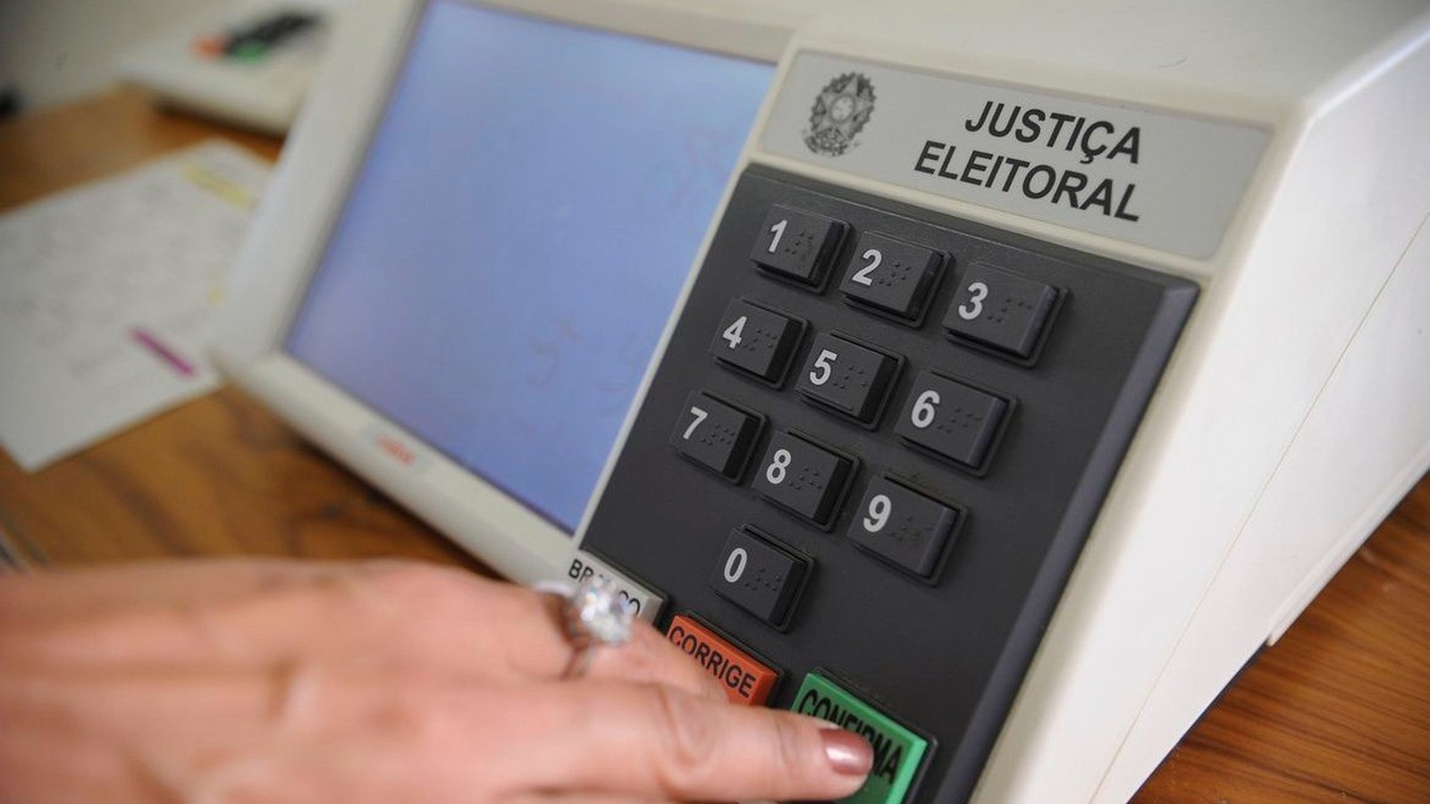 Mão pressiona o botão verde 'CONFIRMA' de uma urna eletrônica da Justiça Eleitoral
