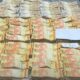 Grandes pilhas de notas de 20 reais brasileiras, presas com elásticos, sobre uma mesa