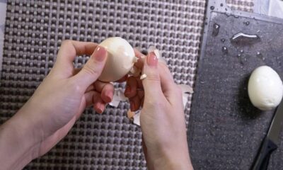 Mãos femininas descascando um ovo cozido, com cascas espalhadas e outro ovo descascado ao lado