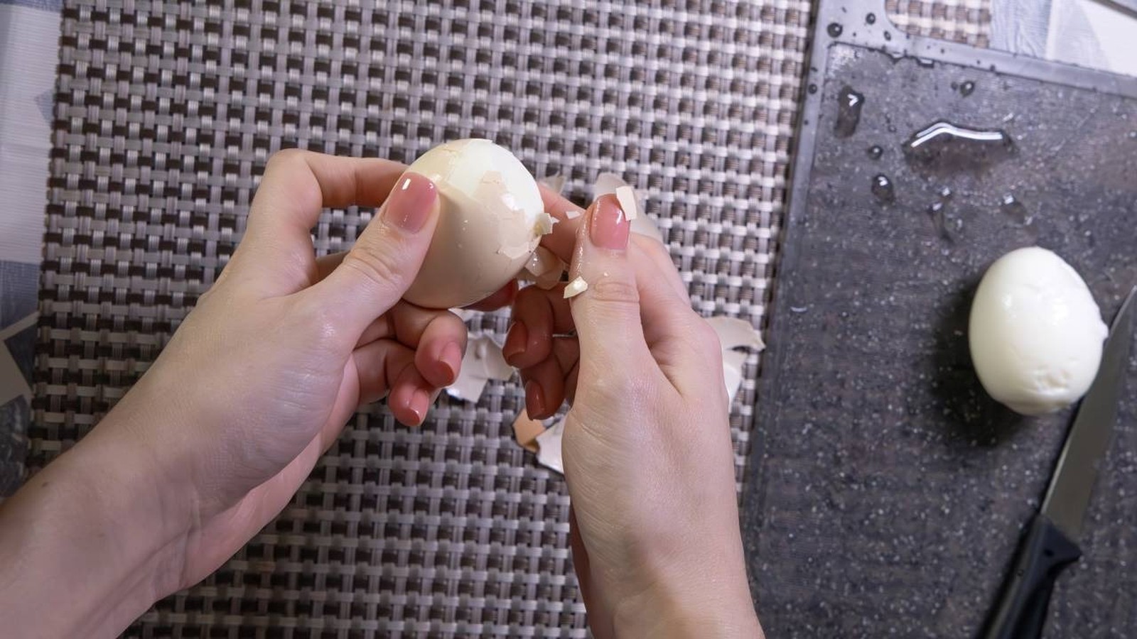 Mãos femininas descascando um ovo cozido, com cascas espalhadas e outro ovo descascado ao lado